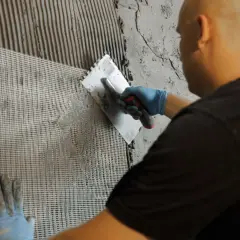 Hand mit blauer Handschuh trägt Mörtel auf ein Gitter auf der wu wand auf.