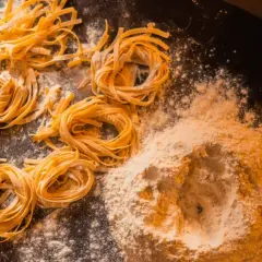 Domowy makaron, jak u babci! Świeże tagliatelle uformowane w gniazda, obok kopczyka mąki. Przepis babci na pyszne danie.