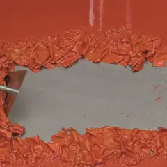 Mit einem Spachtel werden orangefarbene Lackflecken entfernt.