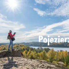 Jesień nad jeziorem. Kobieta z aparatem podziwia krajobraz, szukając ełk atrakcji dla dorosłych. Słońce, chmury i kolorowe drzewa tworzą malowniczy widok.