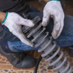 Ręce w rękawiczkach trzymają sprężynę amortyzatora, sprawdzając jej stan.