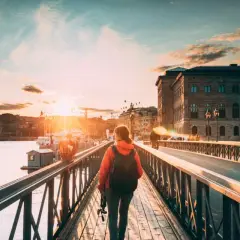 En person med ryggsäck promenerar i Stockholm vid solnedgången över vattnet.