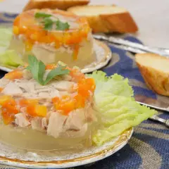 Elegancka ryba w galarecie z marchewką i natką pietruszki, podana na liściu sałaty z pieczywem.