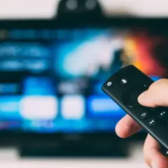 Dłoń trzymająca pilot do telewizora, ekran pokazuje menu. Dowiedz się, jak oglądać TV naziemną przez internet.