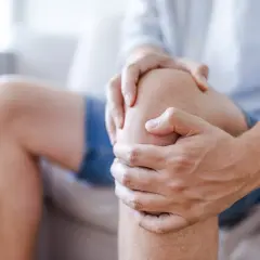 Mężczyzna trzyma się za kolano, odczuwając rwący ból kolana w spoczynku.