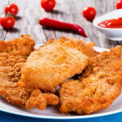 Chrupiące sznycle na białym talerzu, obok pomidorki i papryczka chili. Idealne na obiad!