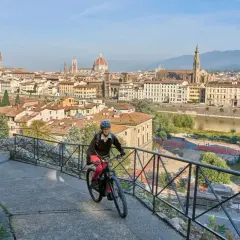 A woman enjoys an Italy bike tour, cycling with Florence's iconic skyline behind her.