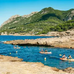 Kajakfahrer erkunden eine felsige Bucht mit türkisfarbenem Wasser und bewaldeten Bergen im Hintergrund. Perfekt für die Frage: wohin auf Mallorca?
