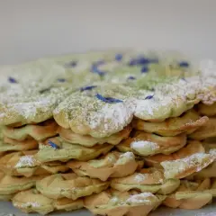 Ein Stapel leckerer Matcha Waffeln, bestäubt mit Puderzucker und verziert mit blauen Blütenblättern.