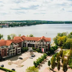 Willa Port w Ostródzie, hotel z widokiem na jezioro, otoczony zielenią i zabudowaniami.