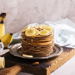 Stos naleśników z plasterkami bananów, idealny pomysł, co zrobić z dojrzałych bananów. Obok kubek i świeże banany.