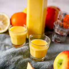 Frische Zutaten für Ingwer Shots selber machen: Zitrone, Orangen, Äpfel und ein Glas voller goldgelbem Shot.