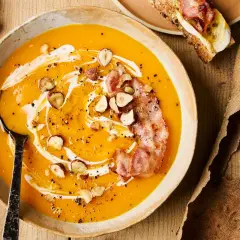 Soupe de courge butternut crémeuse garnie de lardons croustillants, noisettes et filet de crème.