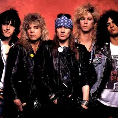 Guns N' Roses członkowie w skórzanych kurtkach i z charakterystycznymi fryzurami. Axl Rose w bandanie, Slash z burzą loków.