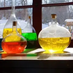 Kolorowe płyny w kolbach, jak uratować zoctowane wino? Słońce odbija się od szkła, tworząc magiczne refleksy.
