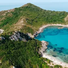 Idealna pogoda na Korfu we wrześniu: turkusowa zatoka, zielone wzgórza i piaszczysta plaża z łódkami.