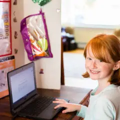 Uśmiechnięta dziewczynka z rudymi włosami uczy się na **chromebooku**. Co to jest? To jej narzędzie do nauki i zabawy.
