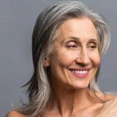 Mujer sonriente con cabello plateado, sus canas brillan con sabiduría y experiencia.