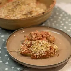 Dos porciones de gnocchi alla romana gratinados con queso, servidos en un plato marrón sobre un mantel de lunares.