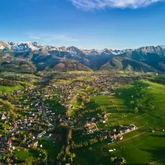Widok na Zakopane i Tatry. Zielone łąki, zabudowania i ośnieżone szczyty tworzą malownicze okolice Zakopanego atrakcje.