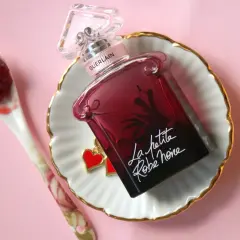 Elegancka buteleczka perfum Guerlain La petite robe noire z uroczymi serduszkami, obok łyżeczka z dżemem.