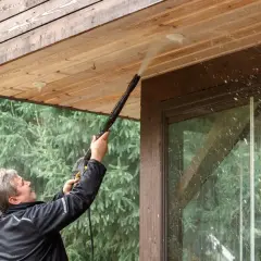Mężczyzna myje drewnianą podbitkę myjką ciśnieniową. Woda rozpryskuje się, pokazując, czy biała podbitka się brudzi.