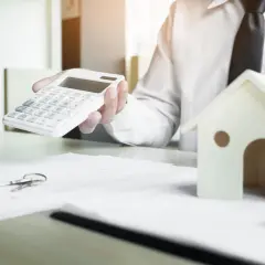 Rozmowa o najmie prywatnym lokalu użytkowego a VAT. Na stole klucze, kalkulator i model domu.