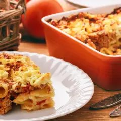 Pyszna zapiekanka makaronowa z mięsem mielonym w sosie śmietanowym, podana na talerzu. Obok naczynie żaroodporne z resztą dania.