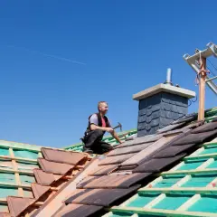 Cieśla układa dachówki, pracując nad nowym dachem. To kluczowy etap, który wpływa na ostateczną cenę dachu.