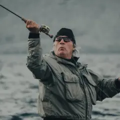 Wędkarz w okularach polaryzacyjnych na ryby, z wędką w ręku, łowi ryby na wzburzonej wodzie.