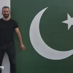 Mężczyzna w czarnym T-shircie i jeansach stoi obok flagi Pakistanu. Marzy o wizie do Pakistanu.