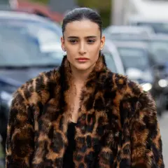 Elegancka kobieta w futrze w panterkę, niczym mob wife, pozuje na tle samochodów.