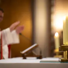 Ksiądz w kościele podczas mszy, zapalone świece. Czy księża płacą podatki? To pytanie nurtuje wielu.