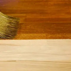 Un pinceau applique un vernis pour foncer du bois, transformant le bois clair en une teinte chaude et profonde.