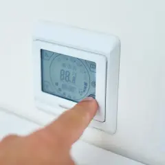 Palec naciska przycisk termostatu, ustawiając idealną temperaturę pieca gazowego.