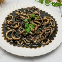 Plato de calamares en su tinta, con anillas tiernas y sabrosas, decorado con perejil fresco. Un clásico irresistible.
