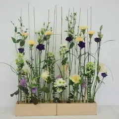 Kompozycja w stylu wegetatywnym we florystyce: delikatne kwiaty, trawy i liście tworzą naturalny, lekki ogród w prostokątnej donicy.