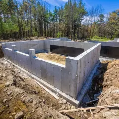 Solidny ruszt fundamentowy z betonu, gotowy na budowę domu. Otoczony ziemią i drzewami, czeka na kolejne etapy prac.