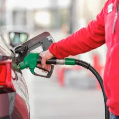 Osoba w czerwonej bluzie dokonuje tankowania samochodu. Zielony pistolet paliwowy jest włożony do baku.