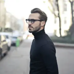 Elegancki mężczyzna w okularach i czarnym golfie, zamyślony, jakby planował zagrywki zakochanego faceta.
