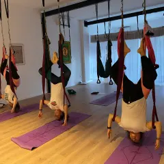 Personas practicando ahimsa yoga en columpios aéreos, invertidas y relajadas.