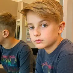 Un bambino di 10 anni con un taglio capelli moderno, capelli biondi sfilati e sfumati ai lati.