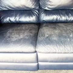 A dark blue leather couch with worn, scuffed seat cushions, showing the need for restoration.