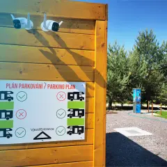 Tablica z planem parkowania dla kamperów, z zaznaczonymi miejscami dozwolonymi i zakazanymi. Dwie kamery monitoringu nadzorują teren.