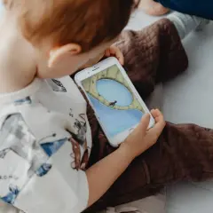 Un niño, absorto en su móvil, parece un niño adicto al móvil. La pantalla muestra un juego con un personaje en un paisaje acuático.