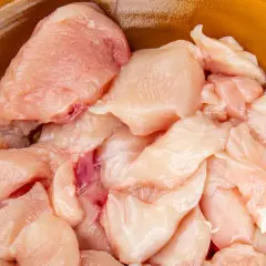 Surowe kawałki piersi kurczaka w pomarańczowej misce.