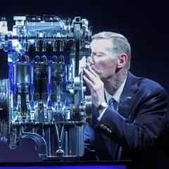 Mężczyzna w garniturze całuje silnik Forda. Wiele osób szuka **1.0 ecoboost opinie** przed zakupem.