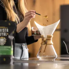Eine Frau gibt mit einem Löffel Kaffeepulver in einen Chemex-Filter. Die richtige **Filterkaffee Menge** ist entscheidend für den perfekten Geschmack.