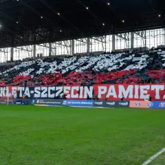 Trybuna stadionu podczas meczu Pogoń Szczecin – Widzew Łódź. Kibice tworzą biało-czerwony transparent "ARMIO WYKLETA-SZCZECIN PAMIĘTA!".