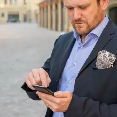 Mężczyzna w garniturze sprawdza telefon, szukając informacji, jak zostać pośrednikiem kredytowym.